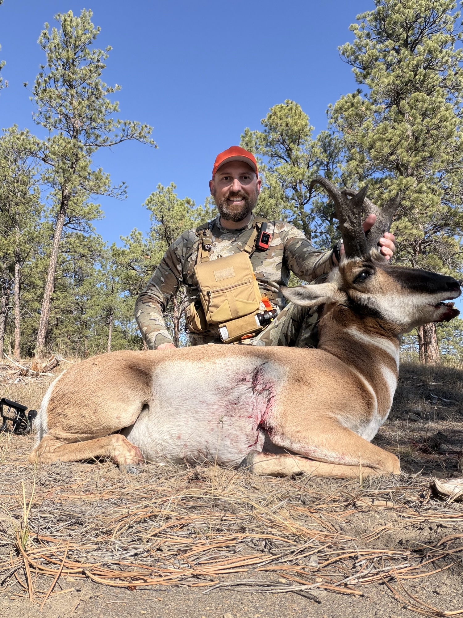 John Mobley in camo with a chest pack and Garmin inReach, kneeling behind a pronghorn buck