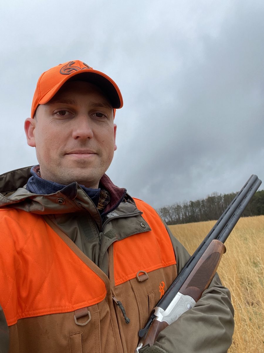 John Mobley in a field with an over-under shotgun, wearing a blaze orange Browning upland vest and cap